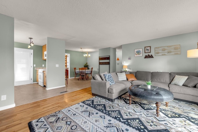 living room with visible vents, an inviting chandelier, a textured ceiling, wood finished floors, and baseboards