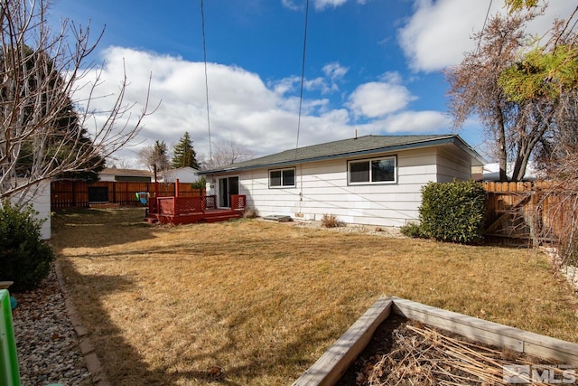 back of property featuring fence, a wooden deck, and a lawn