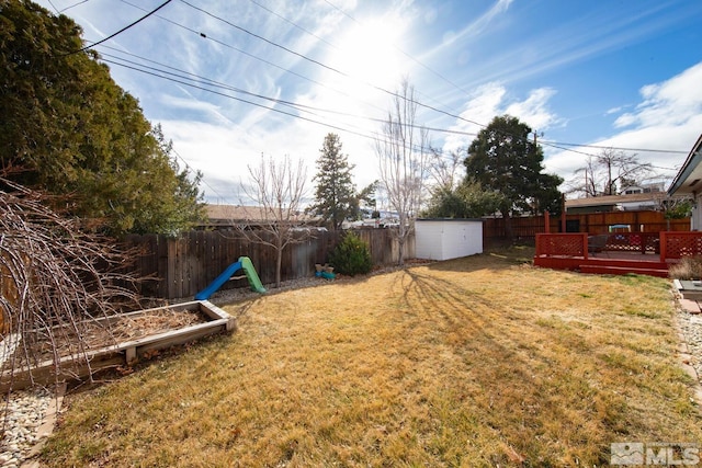 view of yard featuring an outbuilding, a fenced backyard, a deck, and a storage shed