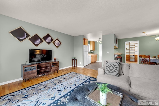 living area with light wood finished floors, a textured ceiling, baseboards, and a notable chandelier