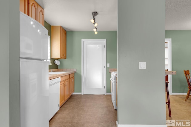 kitchen featuring light countertops, light brown cabinets, a textured ceiling, white appliances, and baseboards