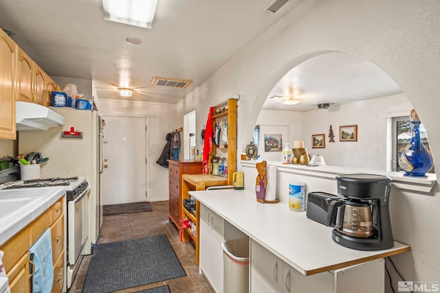 kitchen featuring visible vents, arched walkways, stone finish flooring, white gas range, and under cabinet range hood