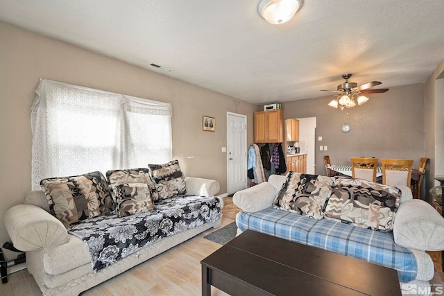 living area featuring visible vents, a textured ceiling, light wood-style flooring, and a ceiling fan