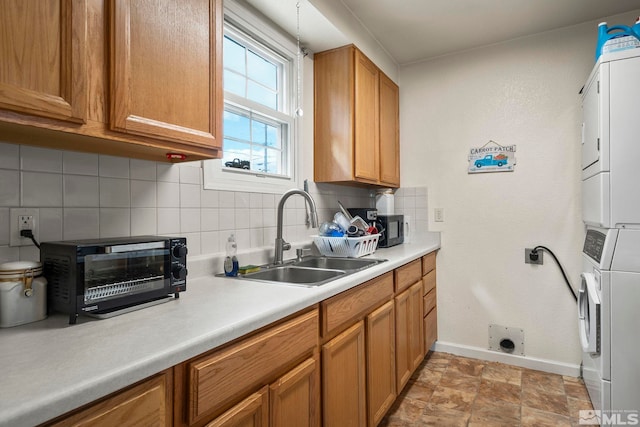 kitchen with a toaster, stacked washer and clothes dryer, a sink, light countertops, and backsplash