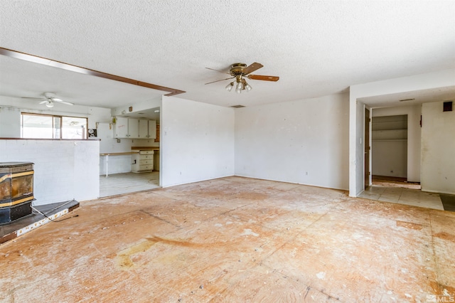 unfurnished living room featuring a wood stove, ceiling fan, and a textured ceiling