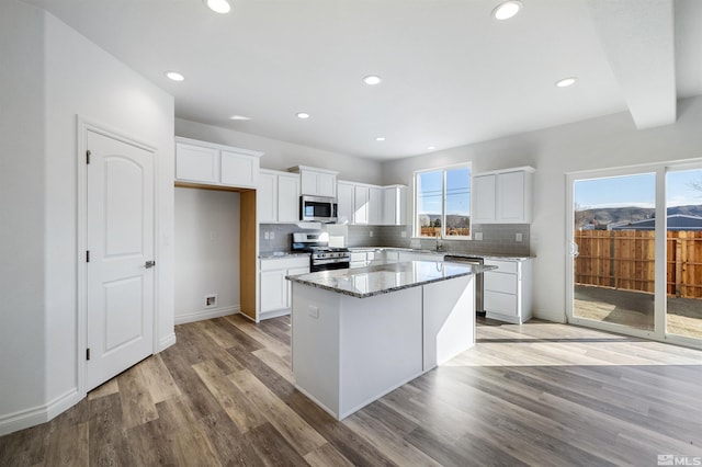 kitchen with light stone counters, stainless steel appliances, a kitchen island, light wood finished floors, and tasteful backsplash