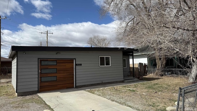 view of outdoor structure with a garage, driveway, and fence