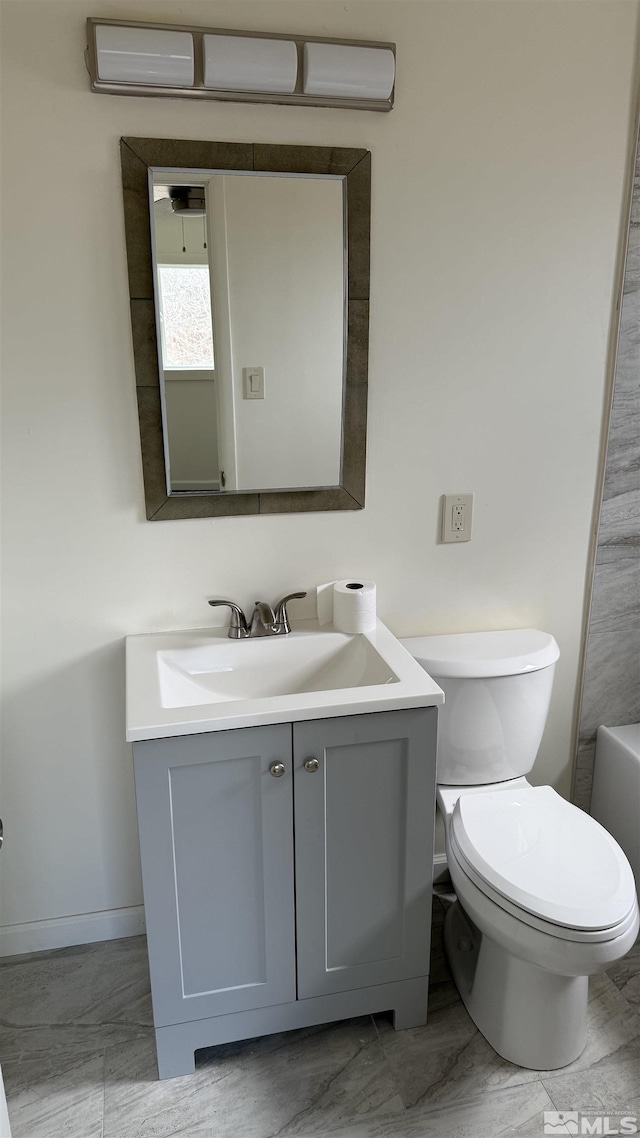 bathroom featuring baseboards, toilet, a bathing tub, marble finish floor, and vanity