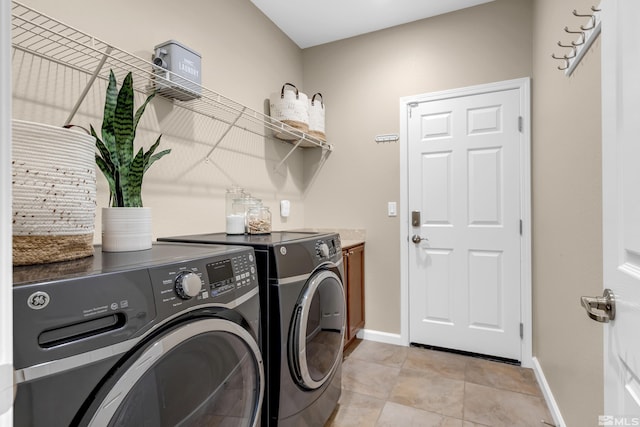 clothes washing area with laundry area, baseboards, washer and clothes dryer, and light tile patterned flooring