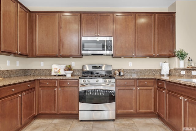 kitchen with brown cabinets, light stone countertops, stainless steel appliances, and light tile patterned flooring