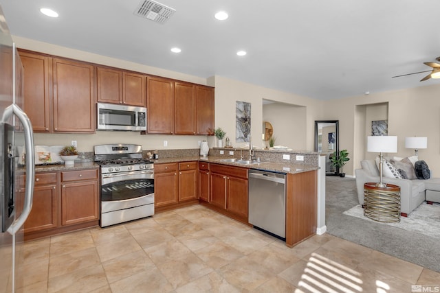 kitchen with visible vents, appliances with stainless steel finishes, brown cabinetry, open floor plan, and a sink