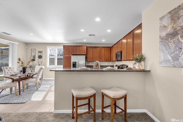 kitchen with visible vents, brown cabinetry, appliances with stainless steel finishes, dark stone countertops, and a peninsula