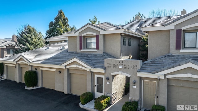 view of property featuring a garage, a tile roof, driveway, and stucco siding