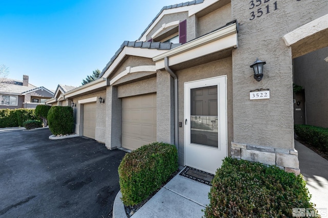 view of exterior entry featuring driveway, an attached garage, and stucco siding