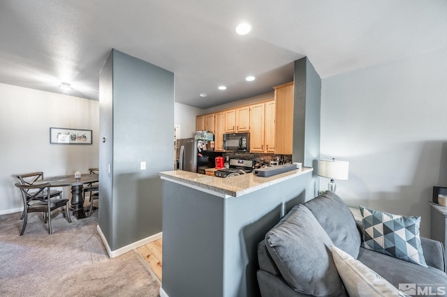 kitchen featuring light carpet, appliances with stainless steel finishes, a peninsula, light countertops, and light brown cabinetry