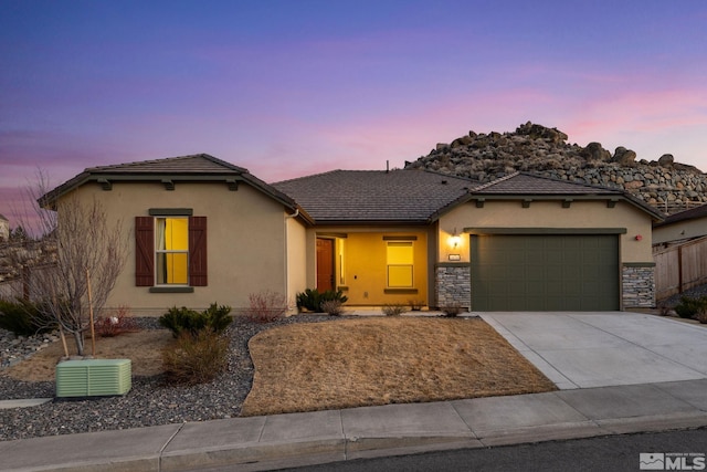 view of front of house featuring an attached garage, stone siding, concrete driveway, and stucco siding