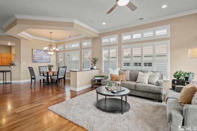 living room with light wood finished floors, visible vents, ornamental molding, baseboards, and ceiling fan with notable chandelier