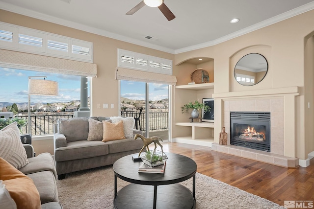 living room featuring visible vents, a tile fireplace, ornamental molding, light wood-style floors, and built in shelves