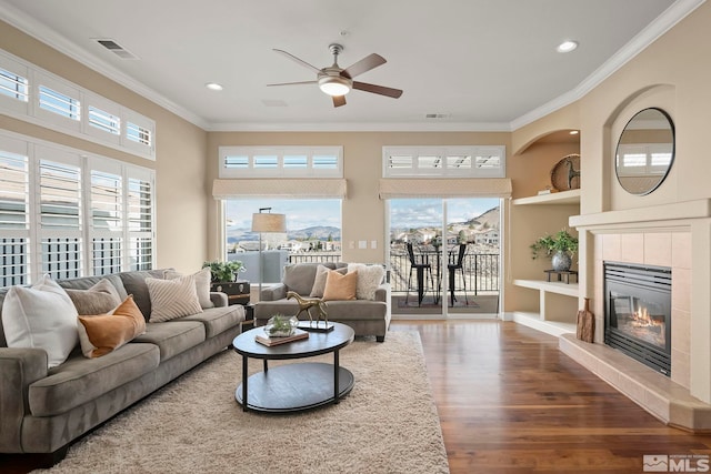 living area with ornamental molding, a tile fireplace, visible vents, and wood finished floors