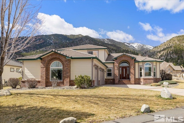 view of front facade with driveway, an attached garage, a mountain view, a front lawn, and brick siding