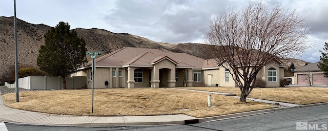 ranch-style home featuring stucco siding, a mountain view, a front yard, and fence