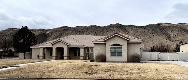 single story home featuring stucco siding, a gate, fence, a mountain view, and a tiled roof