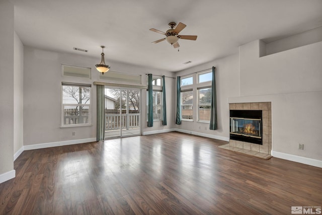 unfurnished living room with a wealth of natural light, a tiled fireplace, wood finished floors, and visible vents