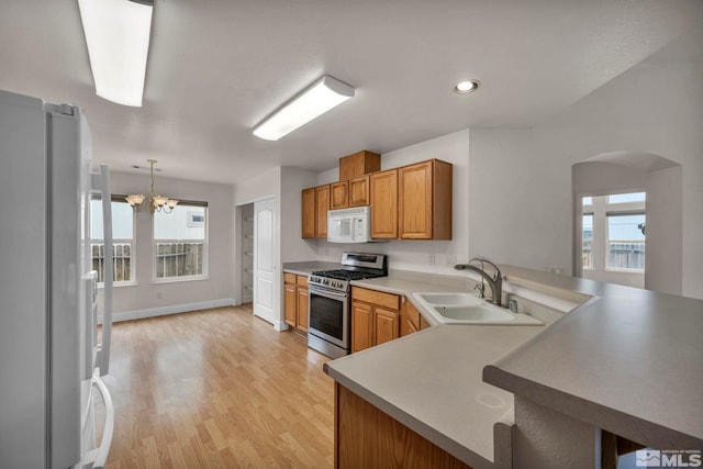 kitchen featuring arched walkways, a peninsula, white appliances, a sink, and light wood finished floors