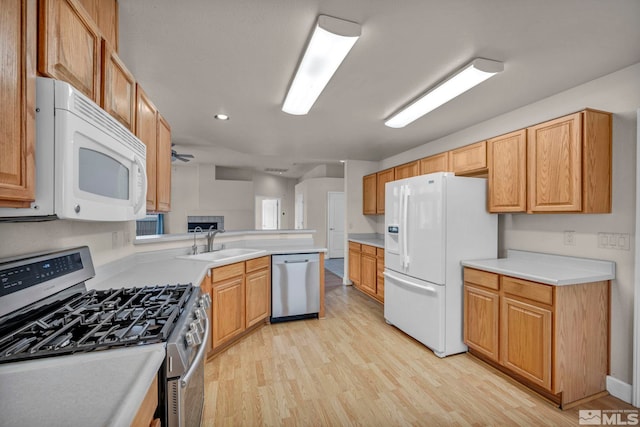 kitchen featuring appliances with stainless steel finishes, a peninsula, light countertops, light wood-style floors, and a sink