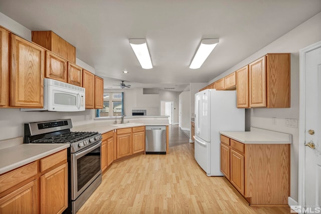 kitchen featuring light wood-style flooring, appliances with stainless steel finishes, a peninsula, light countertops, and a sink