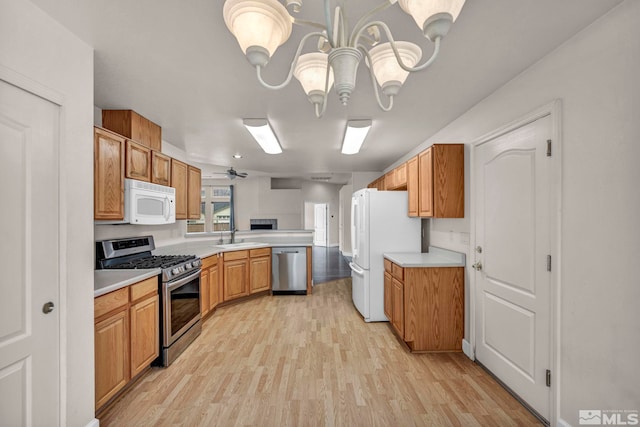 kitchen featuring a peninsula, a sink, light countertops, appliances with stainless steel finishes, and light wood finished floors