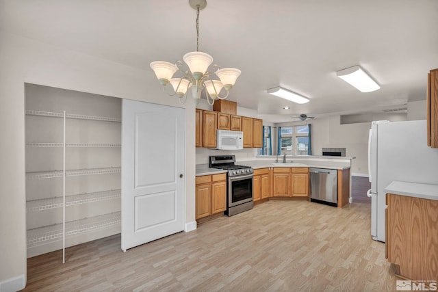 kitchen with light wood-style flooring, a peninsula, stainless steel appliances, light countertops, and a sink