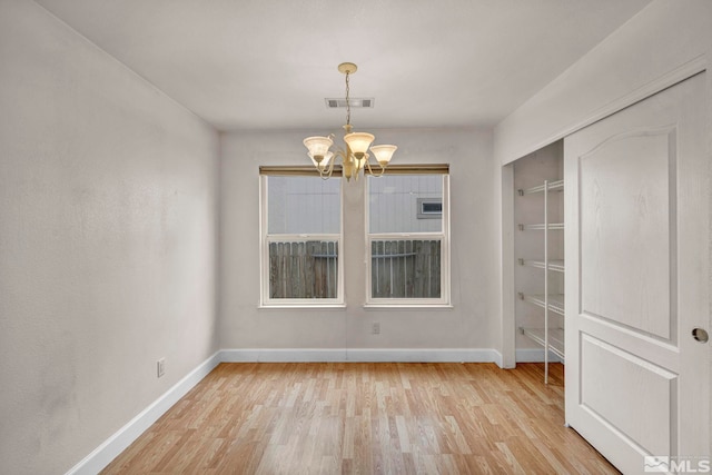 spare room featuring light wood-style floors, baseboards, visible vents, and an inviting chandelier