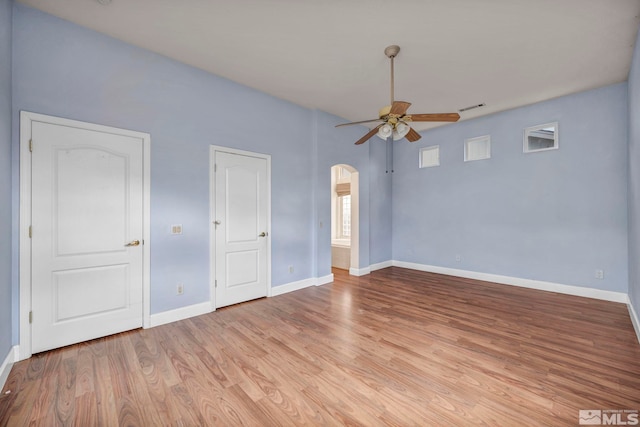 spare room featuring arched walkways, baseboards, light wood-style flooring, and a ceiling fan