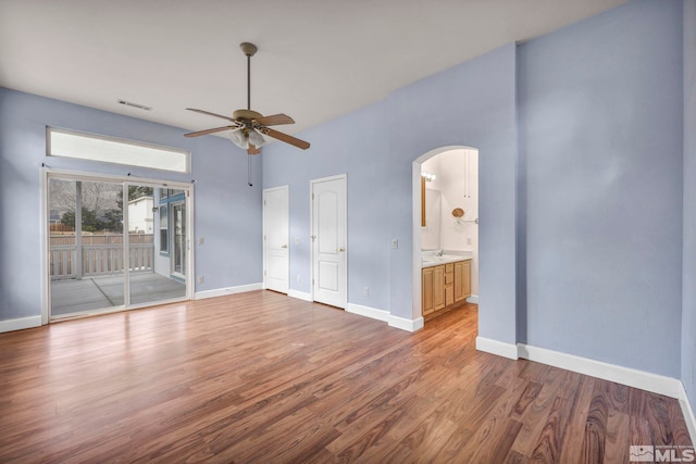 unfurnished bedroom with baseboards, visible vents, arched walkways, wood finished floors, and access to exterior