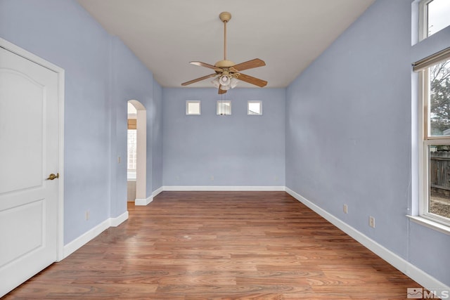 empty room with light wood-style floors, baseboards, arched walkways, and a ceiling fan