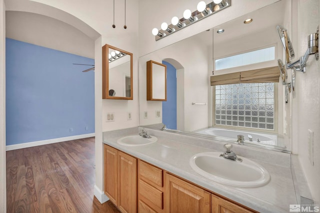 full bath featuring double vanity, a garden tub, a sink, and wood finished floors