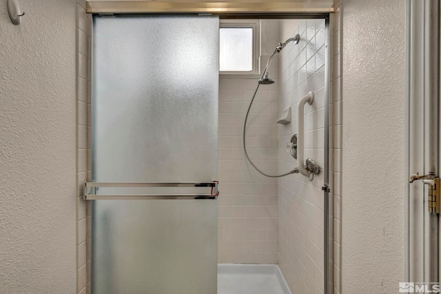 bathroom featuring a textured wall and a stall shower