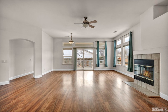 unfurnished living room with arched walkways, a fireplace, baseboards, and wood finished floors