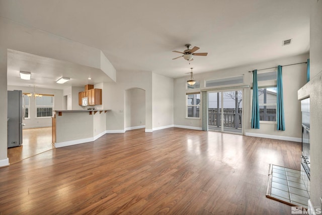 unfurnished living room with baseboards, visible vents, arched walkways, wood finished floors, and ceiling fan with notable chandelier