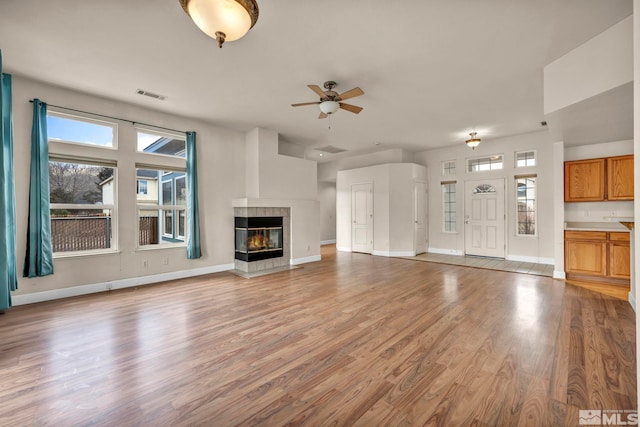 unfurnished living room featuring a fireplace, light wood finished floors, visible vents, a ceiling fan, and baseboards