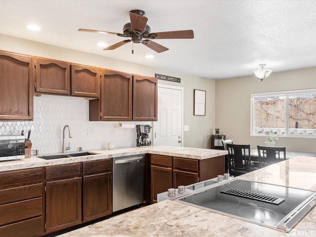 kitchen with a peninsula, a sink, a ceiling fan, appliances with stainless steel finishes, and decorative backsplash