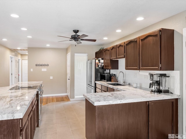 kitchen with dark brown cabinetry, stainless steel appliances, a sink, a ceiling fan, and light countertops