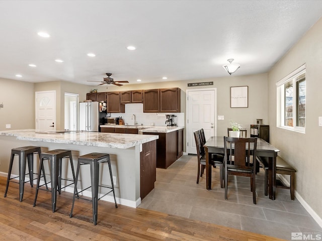 kitchen with a kitchen bar, recessed lighting, light wood-style floors, freestanding refrigerator, and baseboards