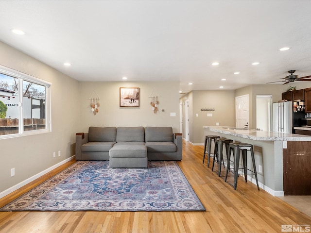 living room featuring light wood-style flooring, baseboards, a ceiling fan, and recessed lighting