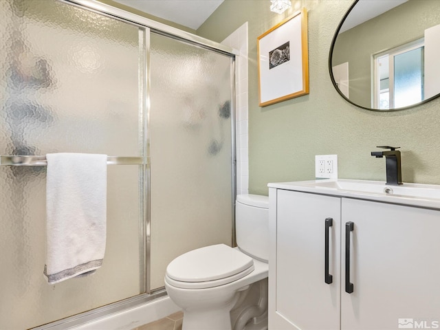 bathroom featuring a stall shower, a textured wall, vanity, and toilet