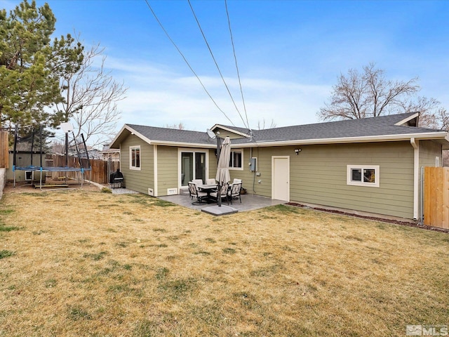 rear view of property with a trampoline, fence, a patio, and a yard