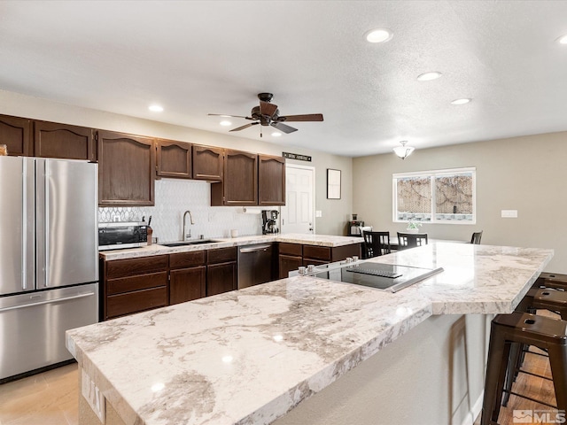 kitchen featuring dark brown cabinetry, a breakfast bar area, a peninsula, stainless steel appliances, and a sink