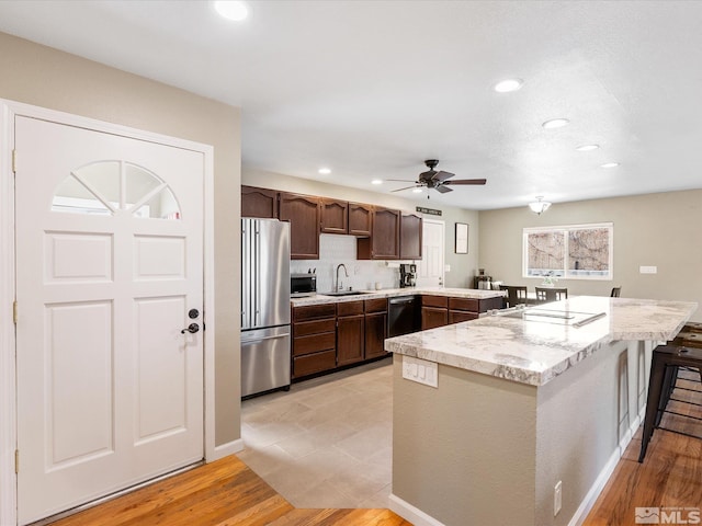 kitchen featuring a peninsula, a sink, light wood-style floors, dark brown cabinets, and appliances with stainless steel finishes