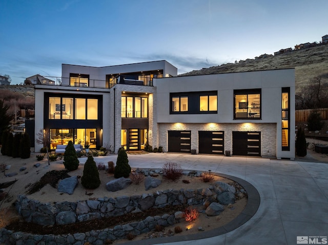 back of property featuring a balcony, a garage, concrete driveway, and stucco siding